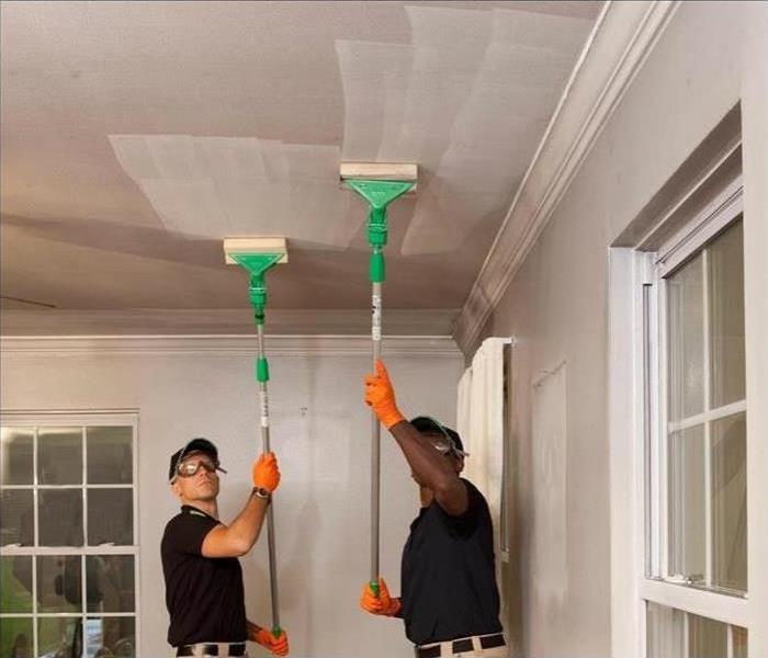 2 men cleaning a white ceiling in a house with white walls and windows 