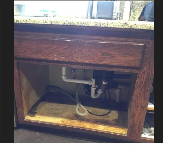sink with brown cabinet opened exposing white plumbing and brown stained bottom of cabinet